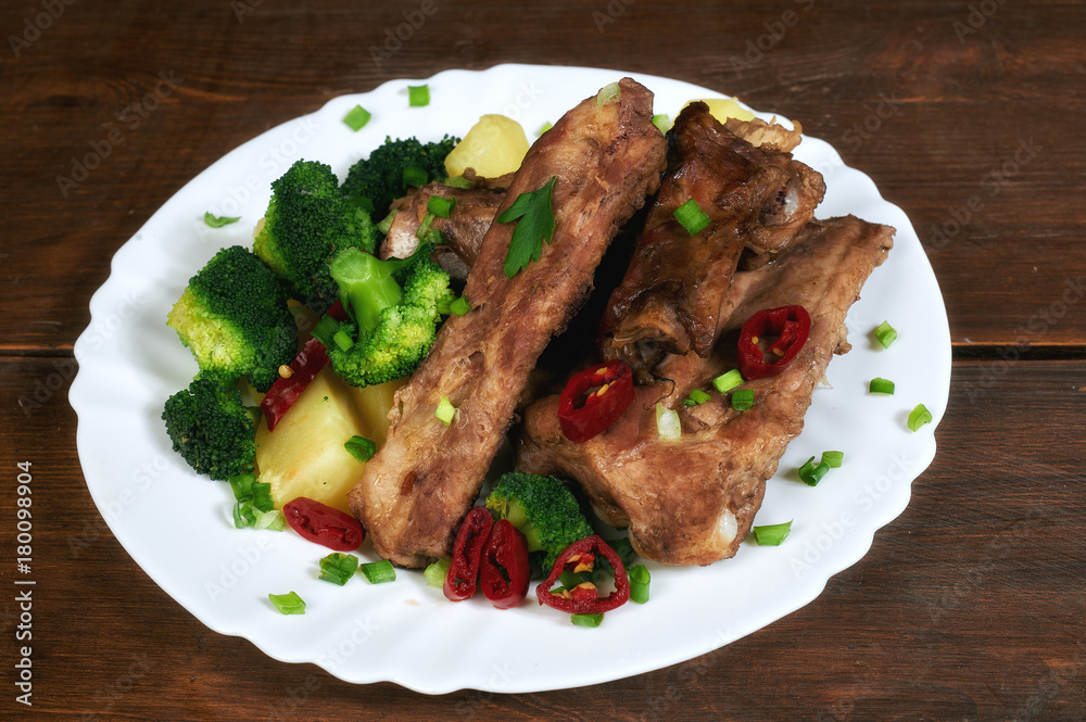 roasted pork ribs with potatoes and broccoli on an old wooden table