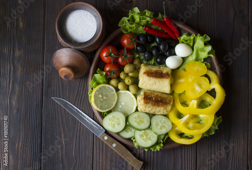 pancakes and fresh organic vegetables  tomatoes  peppers  parsley  lemon  cucumber  chili  spices and olives in a clay plate on the table dark wood