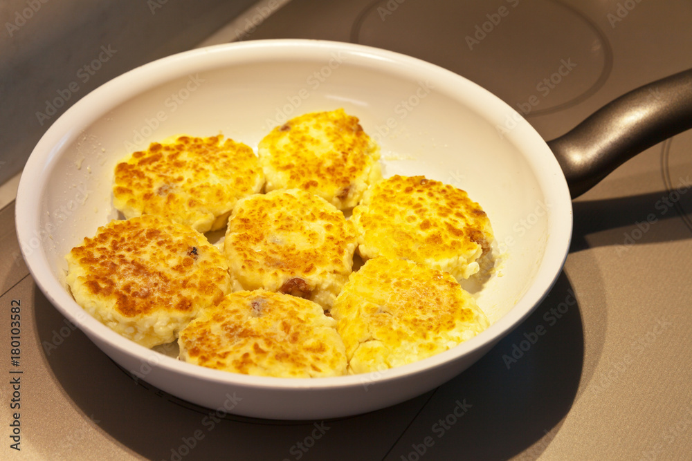 Curd cheese cakes with raisins are fried in a frying pan on an induction cooker Curd cheese cakes with raisins are fried in a frying pan on an induction cooker