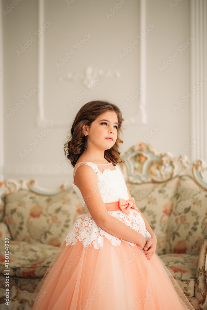 Little beautiful girl with brown hair in a Peach-colored dress. Poses for a photographer Little beautiful girl with brown hair in a Peach-colored dress. Poses for a photographer