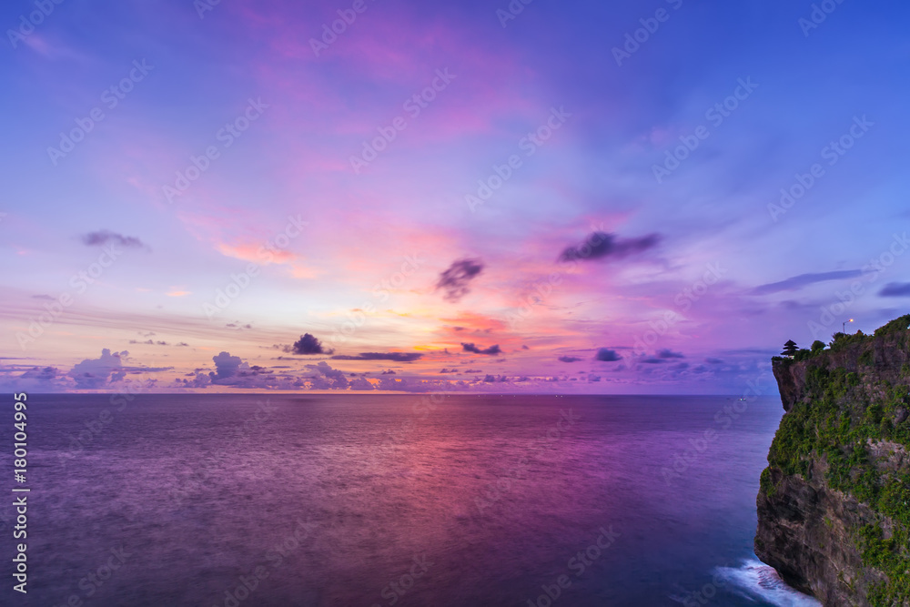 The Hindu temple on a high rock on the Indian Ocean in the southernmost part of the island against the backdrop of beautiful blue orange clouds at sunset. Pura Uluwatu temple, Bali, Indonesia.