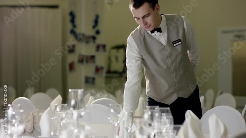 Professional attractive waiter preparing dinner table for wedding celebration at banquet hall at restaurant photo