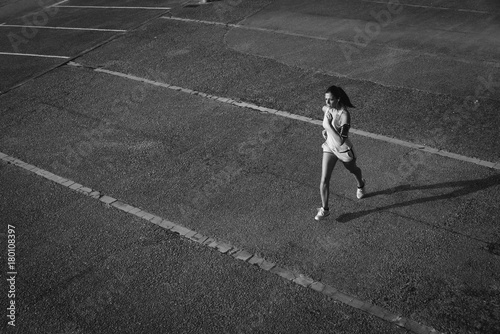 Top view of sporty young fit woman running on urban asphalt. Female athlete training outside in summer.