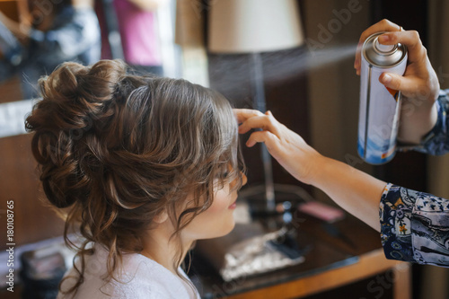 Pretty young bride preparing for wedding at home in the morning. Stylist making hairstyle and apply hairspray on curly hair