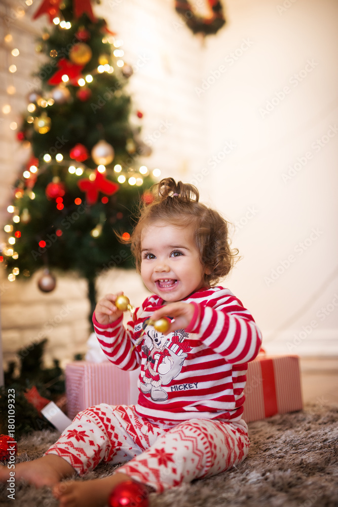 Curly small child girl with ponytail playing with ornaments while sitting on a carpet for Christmas holidays. Curly small child girl with ponytail playing with ornaments while sitting on a carpet for Christmas holidays.