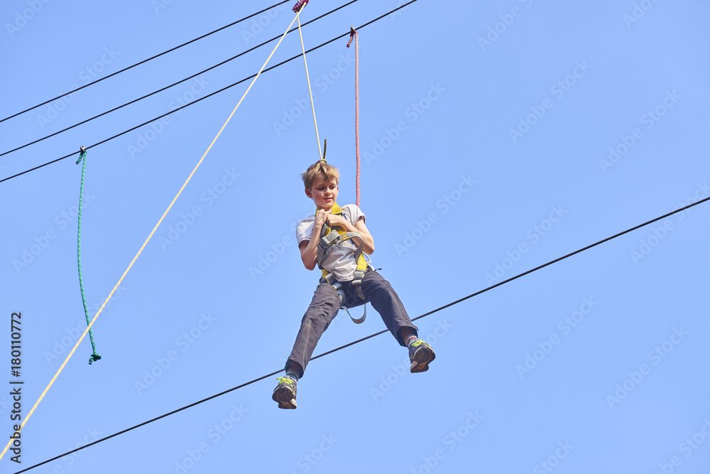 Cute school boy enjoying a sunny day in a climbing adventure activity park. Clear blue sky background. Children summer activities. Cute school boy enjoying a sunny day in a climbing adventure activity park. Clear blue sky background. Children summer activities.