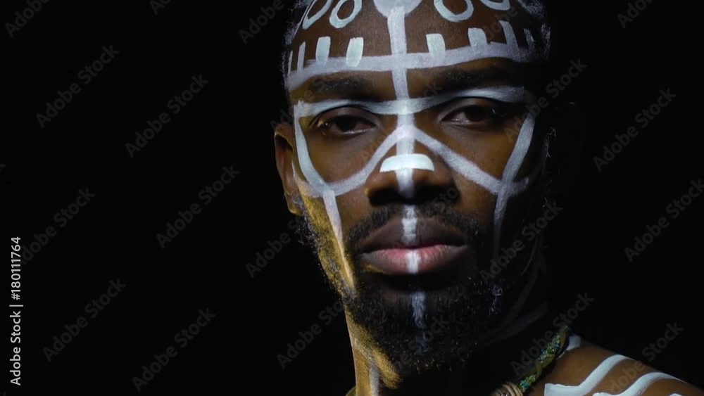 An African American with white patterns on his body and a necklace on his neck turns to the camera An African American with white patterns on his body and a necklace on his neck turns to the camera