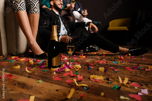 Canvas Print Bottle and glass of champagne on the confetti floor after party with people in b