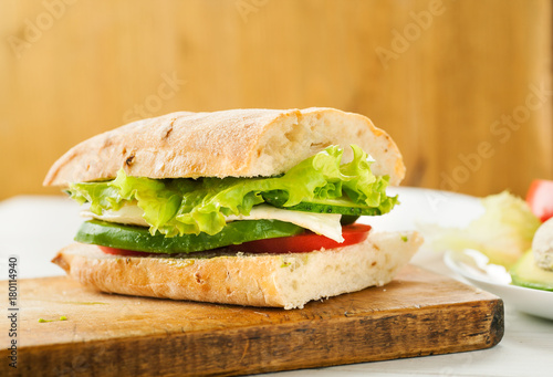 Vegetarian sandwich with avocado, tomato, egg and green salad on a wooden board