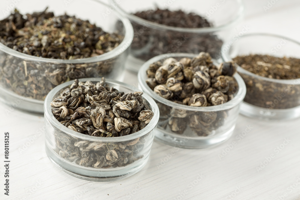 Different dry tea in a small glass dishes on a white wooden table Different dry tea in a small glass dishes on a white wooden table