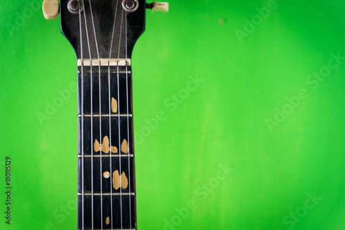 old acoustic guitar on green paint wall background - vintage grunge style with chipped fingerboard