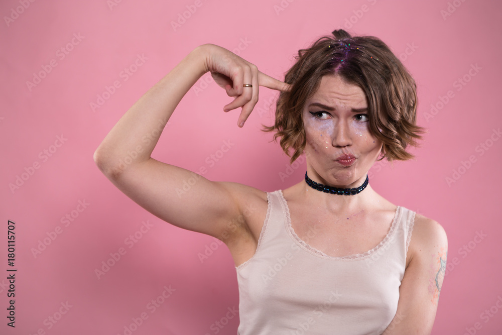 Portrait of young woman in shirt and choker showing screw loose finger gesture. Portrait of young woman in shirt and choker showing screw loose finger gesture.