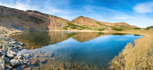 Panorama of mountains lake with reflection in blue water, morning light and shining sun