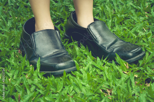 Legs of cute girl wearing black business shoes and standing on green grass in vintage style.