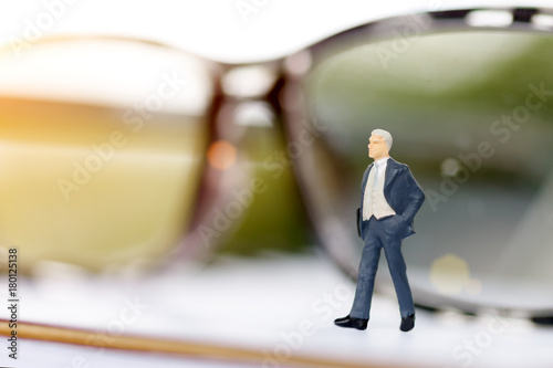 Miniature standing on book with glasses using as background, Business concept..