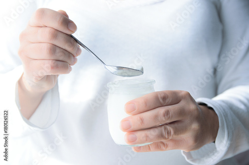 Young woman eating a plain yogurt next to a window in the morning. Empty copy space for Editor's text