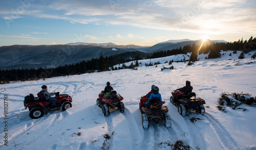 Group of people sitting on off-road quad bikes, enjoying beautiful sunset in the the mountains in winter