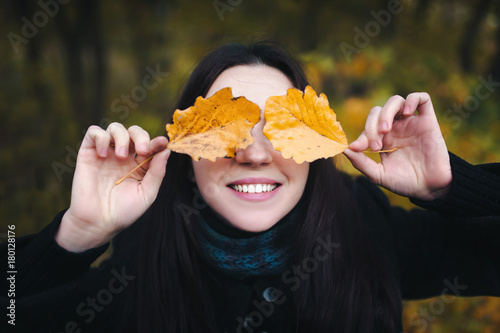 Beautiful young woman closed eyes with autumn leaves. Girl smiling at camera. Outdoor. Holidays. Glasses made from autumn leaves.
