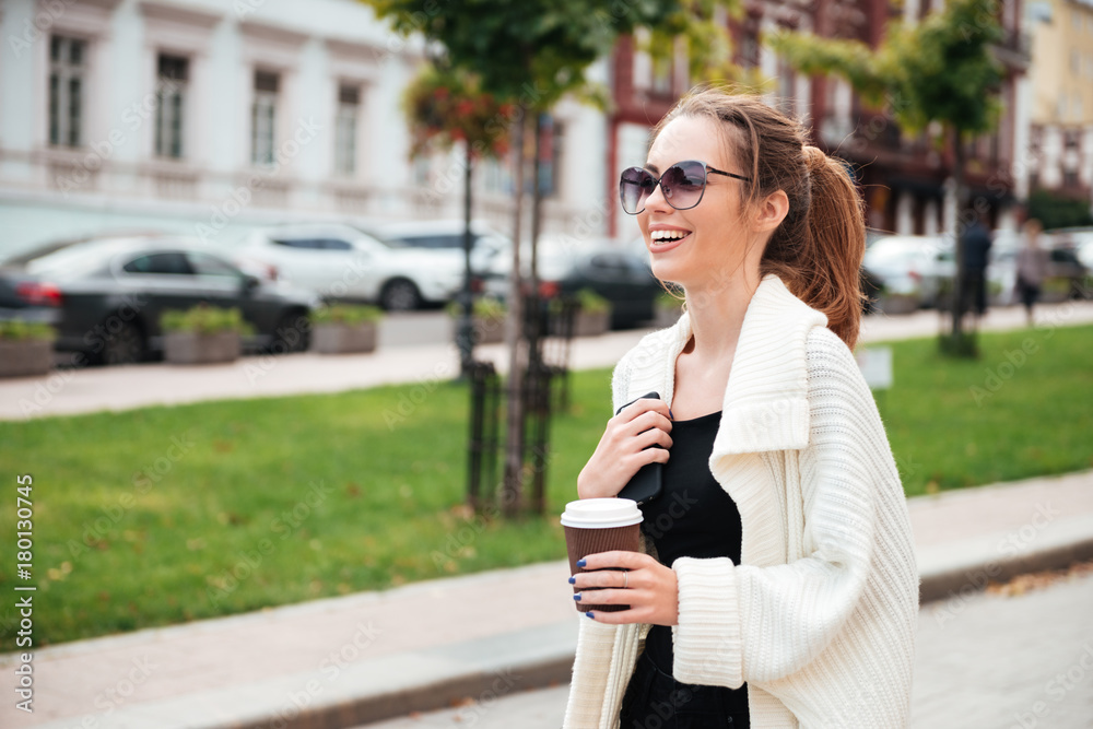 Young cheerful lady walking outdoors drinking coffee