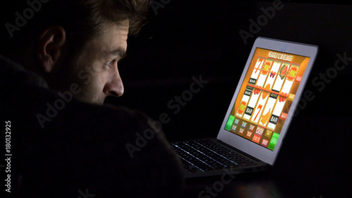 Konstfotografi Gambling addicted man with glasses in front of online casino slot machine on laptop computer at night - loosing his money