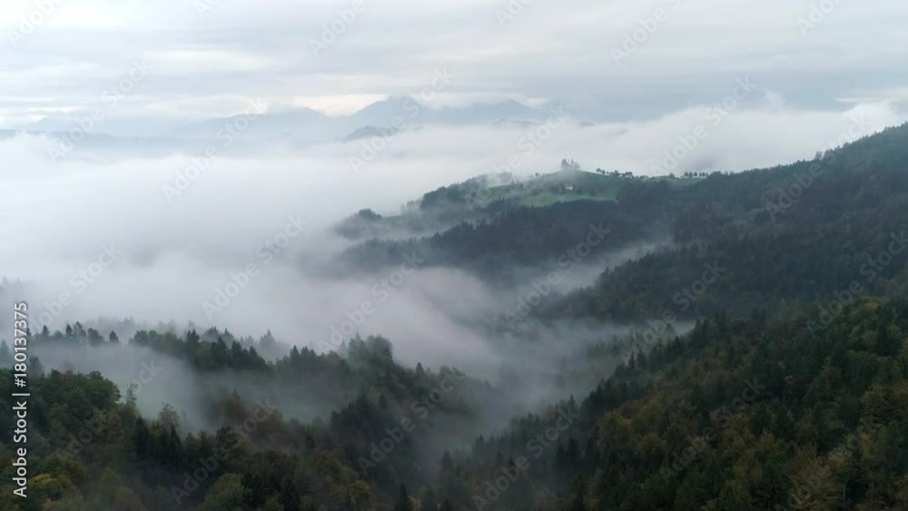 Fast flying aerial view over foggy pine tree forest moving towards hill tops standing above the clouds in Skofja Loka Slvenia. Fast flying aerial view over foggy pine tree forest moving towards hill tops standing above the clouds in Skofja Loka Slvenia.