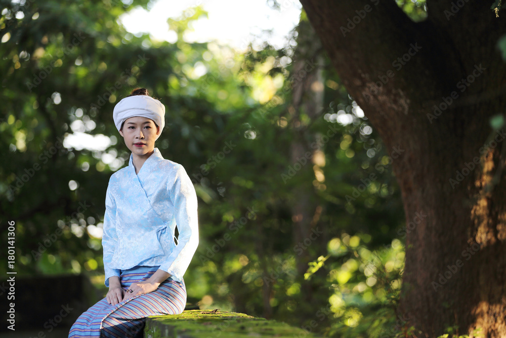 Portrait of thai young woman with traditional thai dress sit in thai temple with tree and sunrise Portrait of thai young woman with traditional thai dress sit in thai temple with tree and sunrise