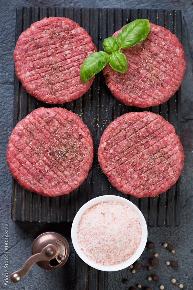 Raw seasoned beef burger cutlets on a black wooden chopping board ready to be cooked, above view, vertical shot Raw seasoned beef burger cutlets on a black wooden chopping board ready to be cooked, above view, vertical shot