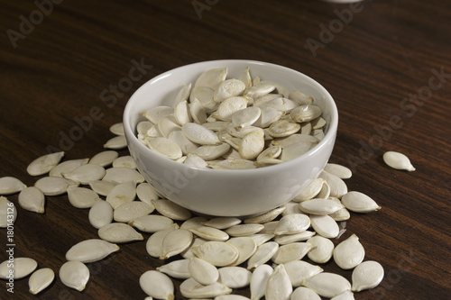 Vegan food. Raw pumpkin seeds for roasting in a white dish. Wooden background.