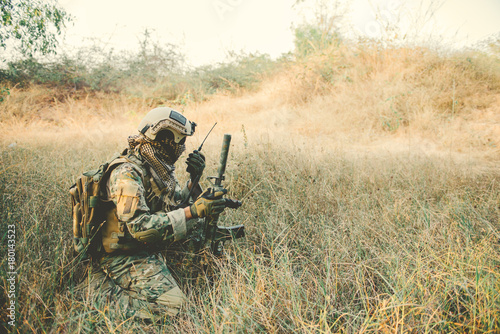 Obraz na plátně Soldier with gun in had sit in the forest,He's using walkie talkie to call for b