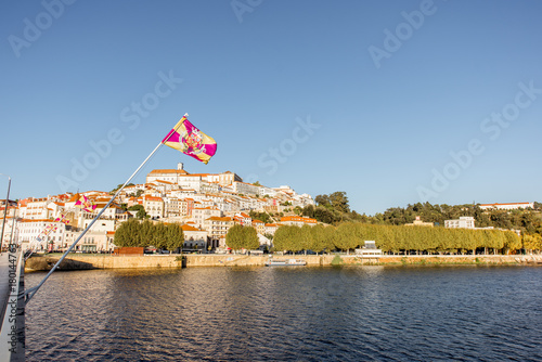 Cityscape view on the old town of Coimbra city with Mondego river and flag during the sunny day in the central Portugal