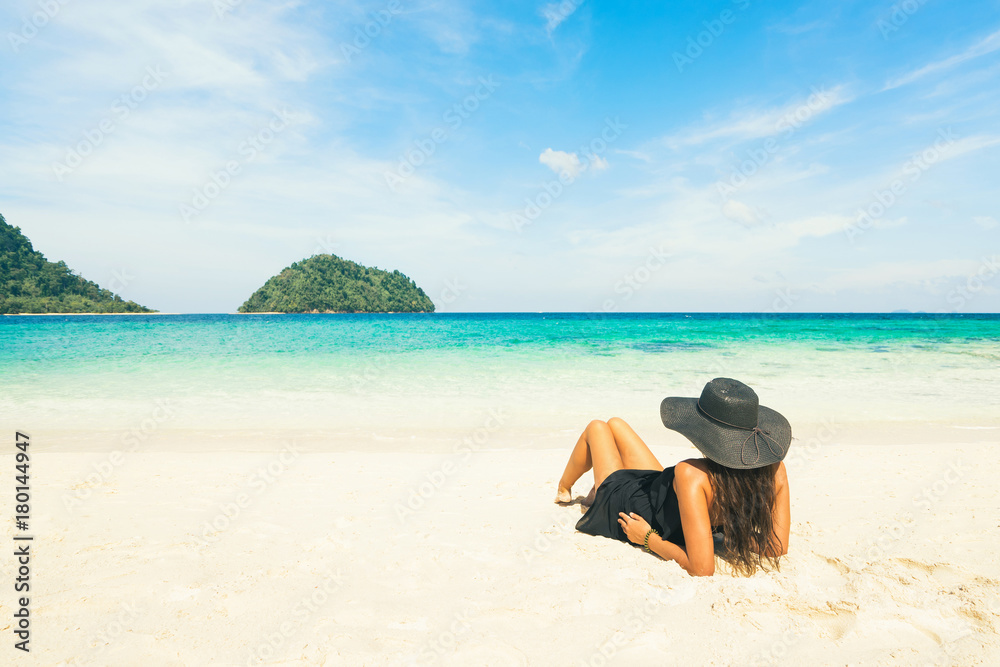 Vacation concept: woman in black hat on beautiful beach looking on island in blue water.