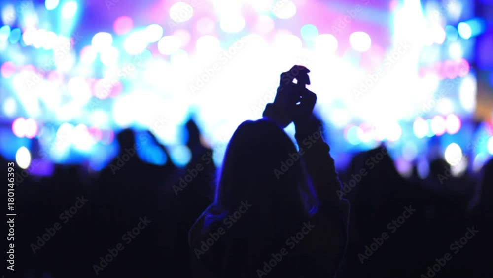 Dancing girl fan silhouettes on concert flashing light cheerful hands in air