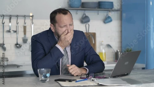 Sick, ill businessman with laptop by the table at home
