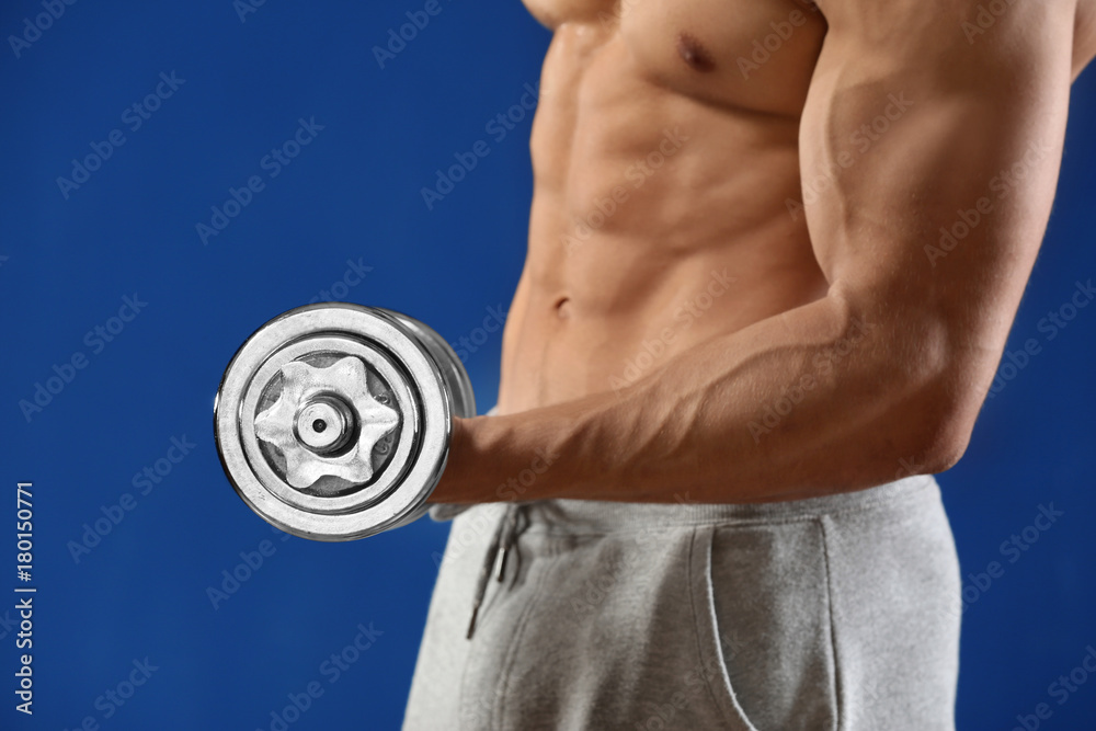 Muscular young man with dumbbell on color background