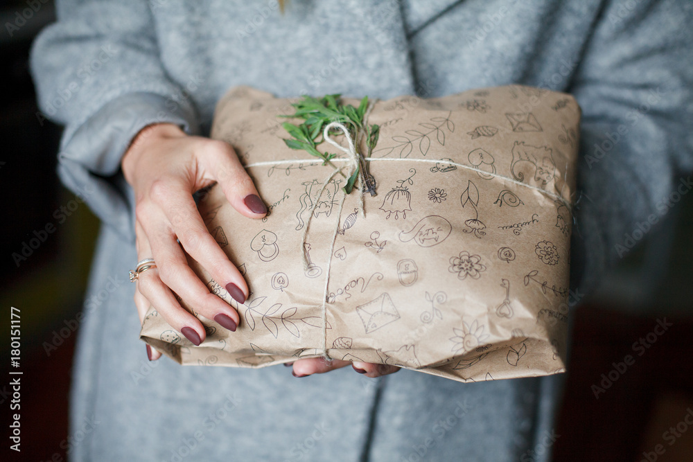 Obraz premium Hands in a gray coat hold a gift, New Year, preparing a gift, packaged in a rustic style, rosemary