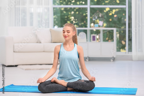 Young woman in sportswear meditating indoors