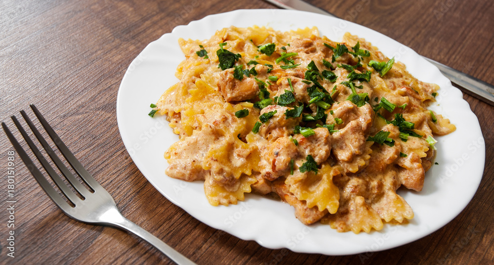 Sliced fried chicken fillet in a creamy sauce. with farfalle pasta. in plate on a wooden background Sliced fried chicken fillet in a creamy sauce. with farfalle pasta. in plate on a wooden background