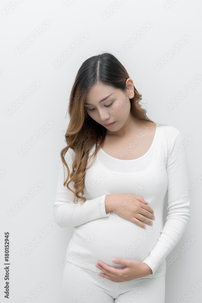 A pregnant woman in white dress standing holding her belly. A pregnant woman in white dress standing holding her belly.