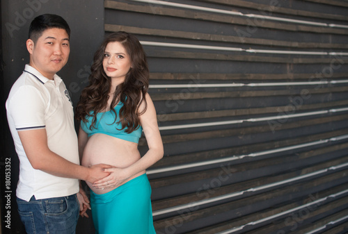 A pregnant young woman and a man are standing side by side, the man put his hand on his stomach. Happiness. Expectation. The blue skirt.