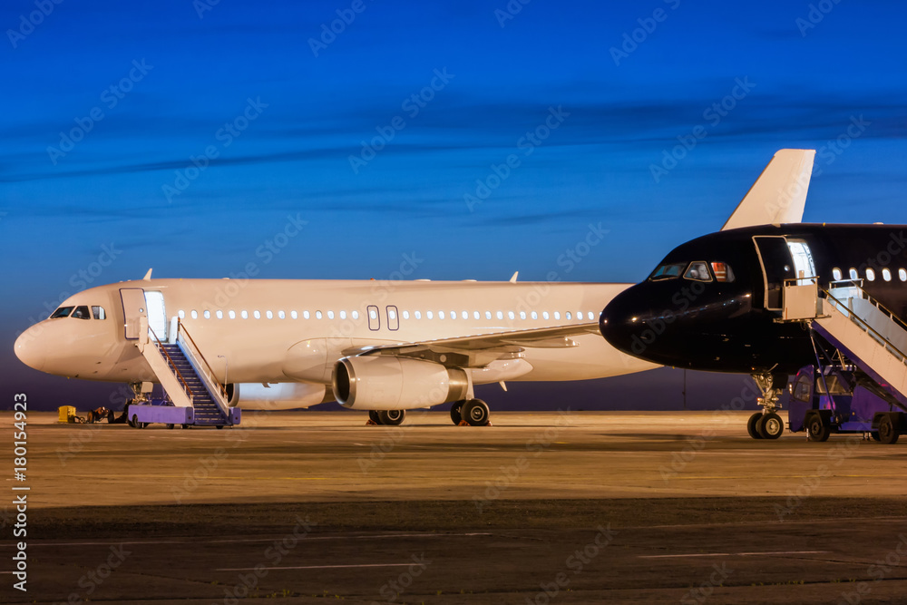 Obraz premium White and black passenger airplanes on the apron of the airport at dusk