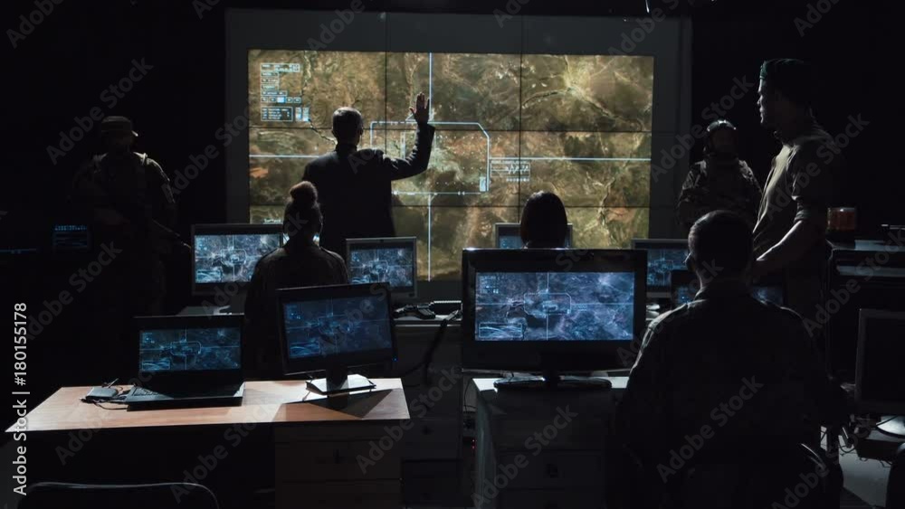 Group of soldiers or spies in dark room with large monitors and advanced satellite communication technology launching a missle. Includes flashing yellow light.