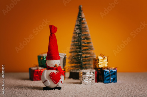Happy snowman, christmas tree and gifts over snowy floor and golden background. © daviles