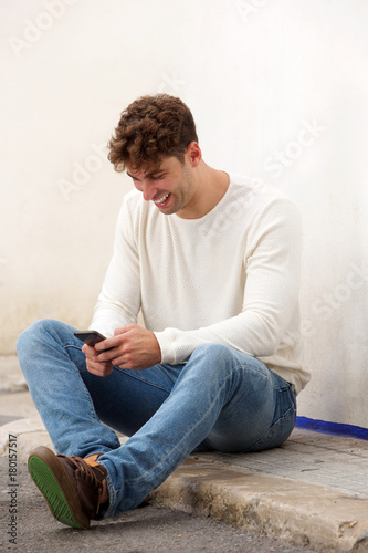 laughing man sitting on ground with mobile phone