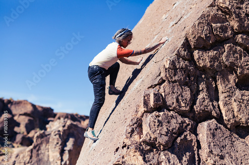 Petite asian woman rock climbing outdoors ascends a sloped stone face with no safety gear