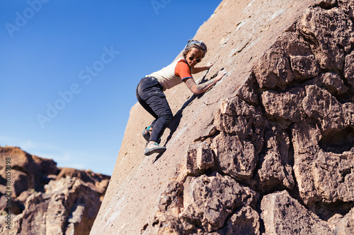 Petite asian woman rock climbing outdoors ascends a sloped stone face with no safety gear