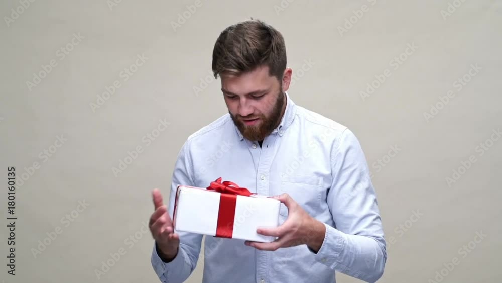 Intrigued bearded man in shirt holding gift over gray background Intrigued bearded man in shirt holding gift over gray background