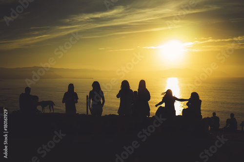 Group of young friends on background beach ocean sunrise, silhouette romantic people dances looking on rear view evening seascape, happy hipster enjoy sunset together, travel holidays vacation