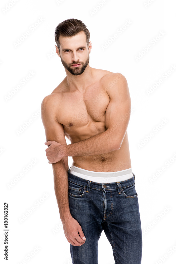 Shirtless and sensual. Handsome shirtless young man in jeans looking at camera while standing against white background.