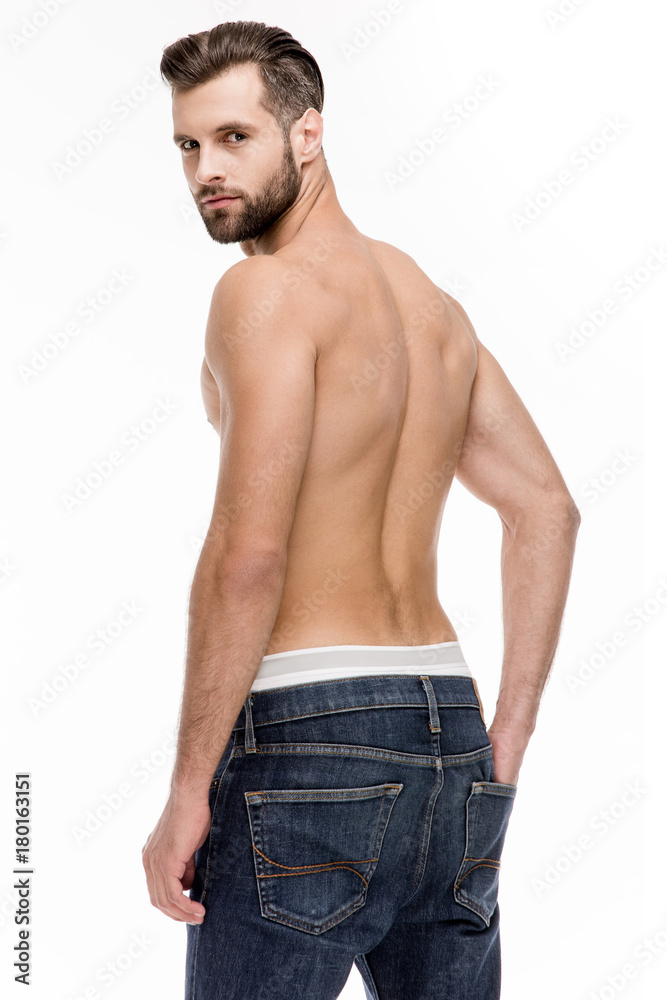 Sexy back. Rear view of young shirtless man in jeans looking at camera while standing against white background.