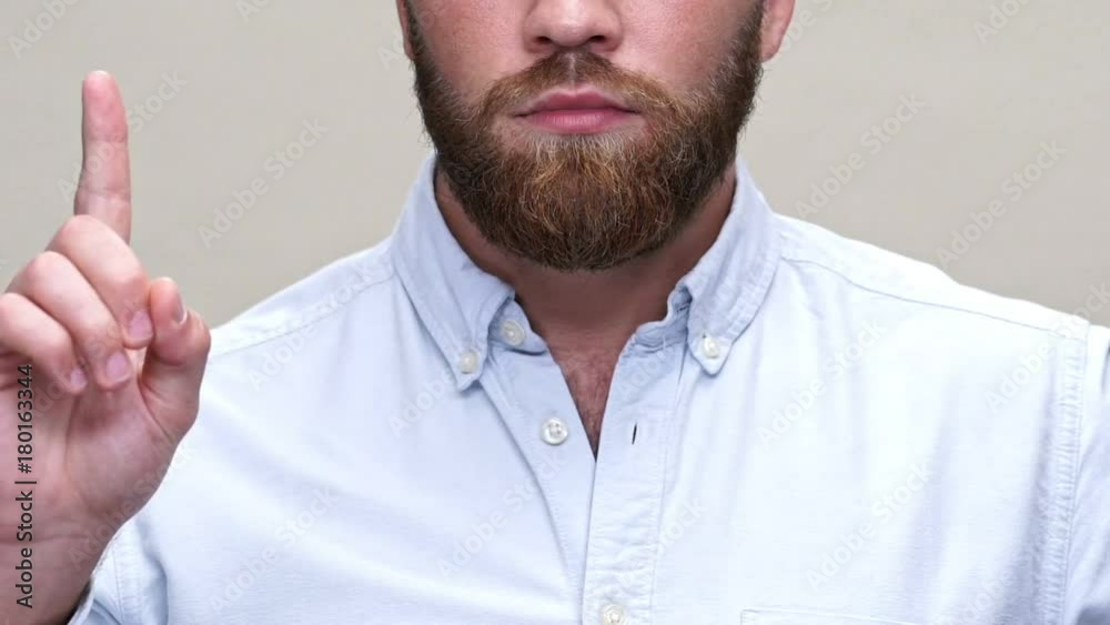 Cropped close up view of calm bearded man in shirt showing dissenting gesture over gray background Cropped close up view of calm bearded man in shirt showing dissenting gesture over gray background
